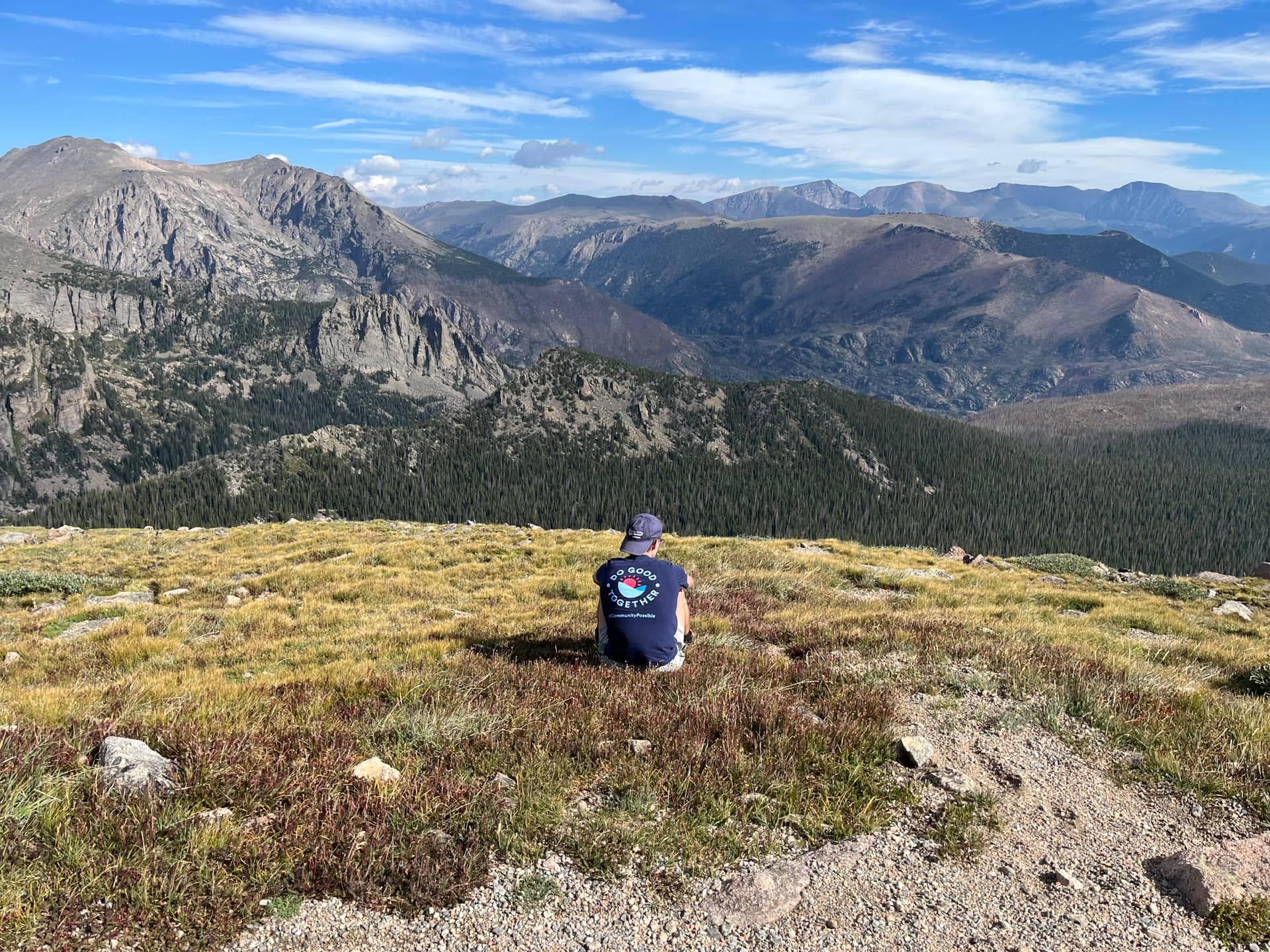 Mathom Johnson sitting on a grassy alpine ridge, looking out over a forested valley and mountain range